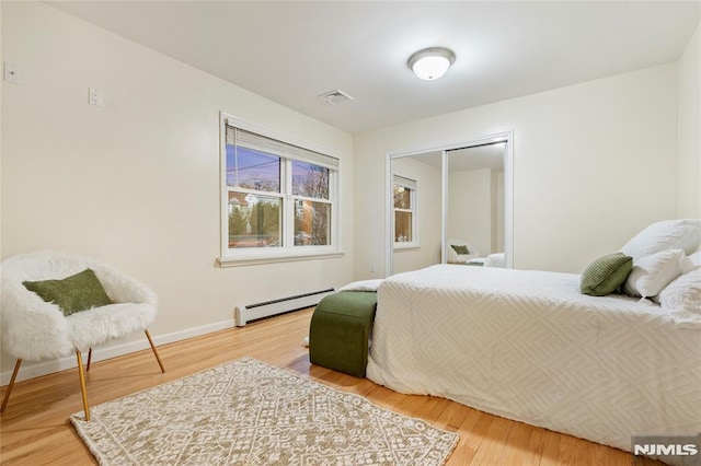 bedroom with a closet, wood-type flooring, and a baseboard heating unit