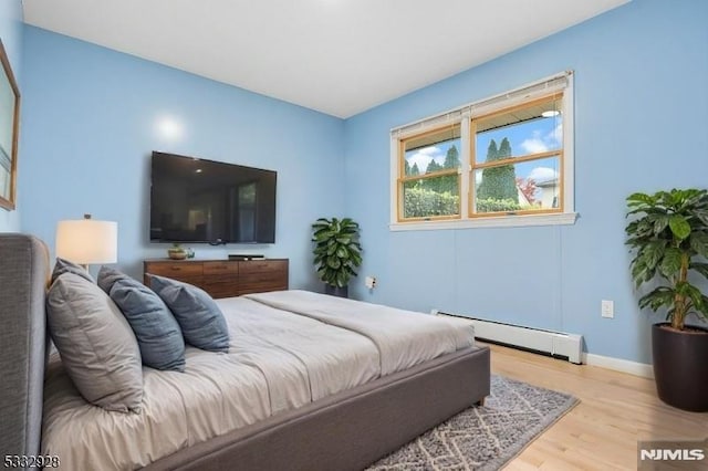 bedroom with a baseboard heating unit and light wood-type flooring