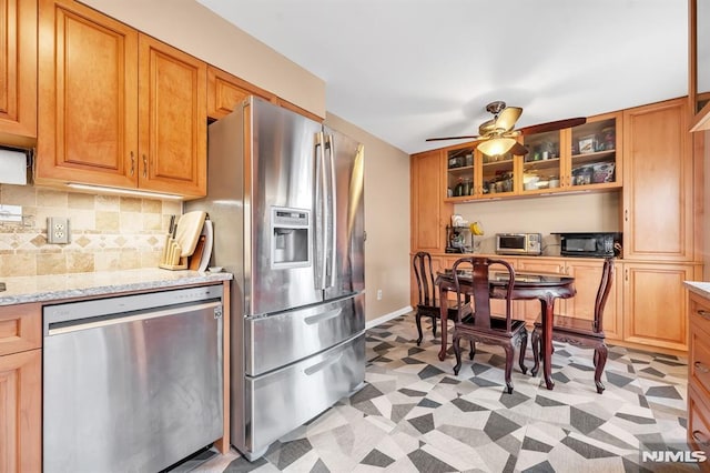 kitchen featuring stainless steel appliances, ceiling fan, tasteful backsplash, and light stone counters