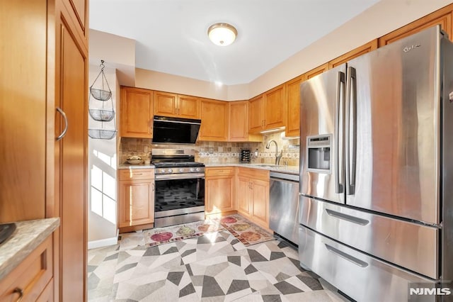 kitchen with light stone countertops, stainless steel appliances, light brown cabinetry, backsplash, and sink