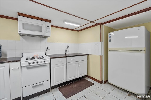 kitchen with white appliances, light tile patterned flooring, tile walls, and white cabinetry