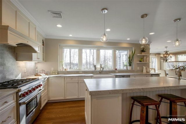 kitchen with a center island, hanging light fixtures, high end stainless steel range oven, white cabinets, and sink