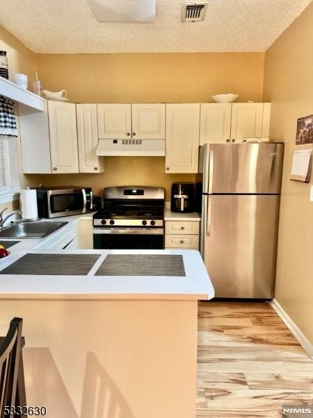 kitchen featuring a textured ceiling, light hardwood / wood-style flooring, stainless steel appliances, white cabinetry, and sink