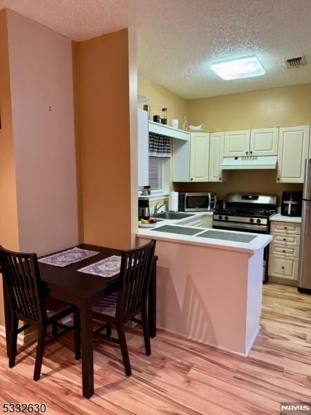 kitchen featuring appliances with stainless steel finishes, a textured ceiling, light hardwood / wood-style flooring, and kitchen peninsula