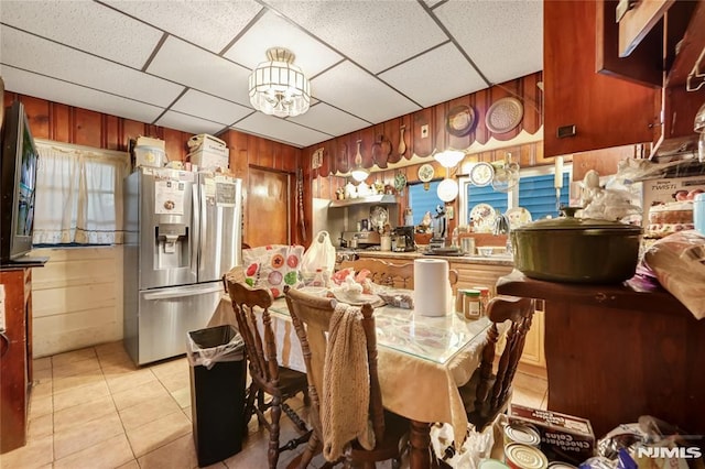 dining room featuring a drop ceiling, light tile patterned floors, and wood walls