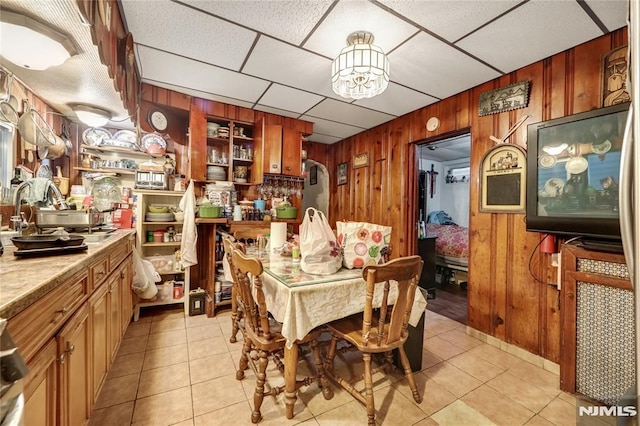 dining room with a drop ceiling, wooden walls, and light tile patterned floors