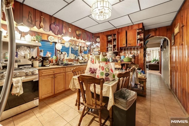 kitchen with gas range, light tile patterned floors, a notable chandelier, wood walls, and a drop ceiling