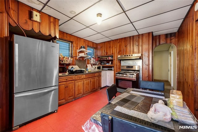 kitchen with appliances with stainless steel finishes, a paneled ceiling, and wooden walls