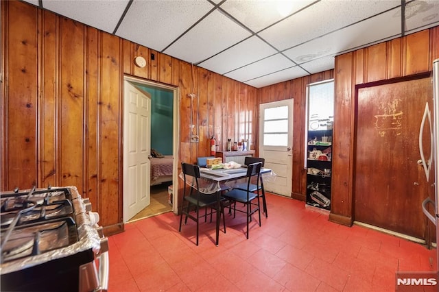 dining room with a paneled ceiling and wood walls