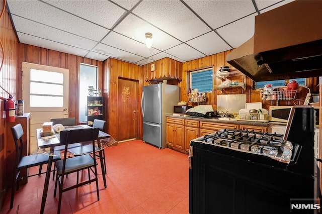 kitchen with island range hood, sink, a paneled ceiling, black appliances, and wooden walls