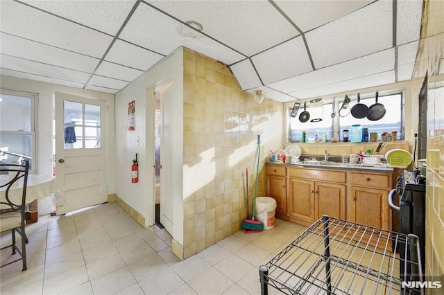 interior space featuring sink, a paneled ceiling, light tile patterned floors, and tile walls