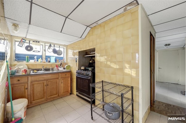 kitchen with a paneled ceiling, sink, tile walls, light tile patterned flooring, and black range with gas stovetop