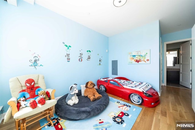 bedroom with connected bathroom, hardwood / wood-style flooring, and electric panel