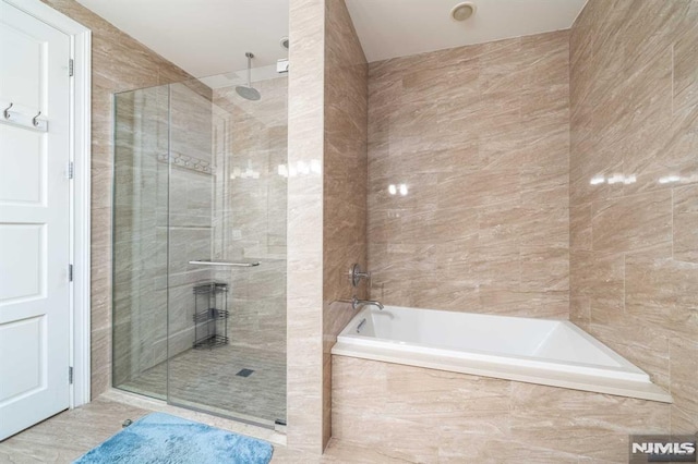 bathroom featuring shower with separate bathtub and tile walls