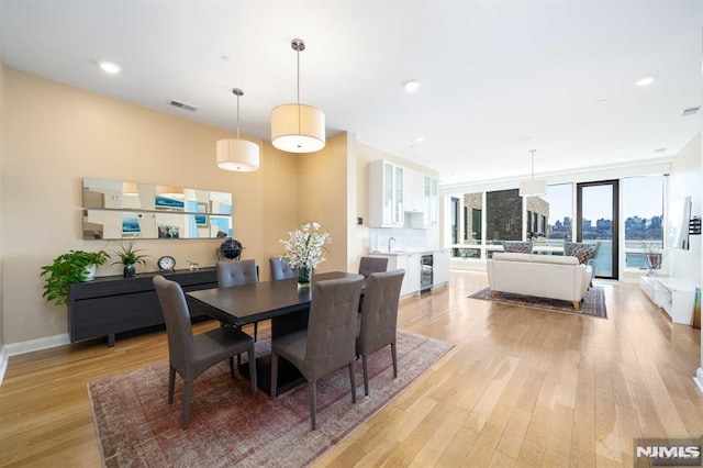 dining area featuring light hardwood / wood-style floors, floor to ceiling windows, sink, and wine cooler