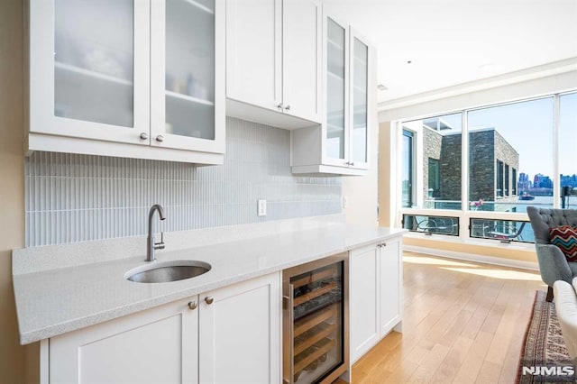 kitchen featuring sink, white cabinetry, light wood-type flooring, beverage cooler, and backsplash