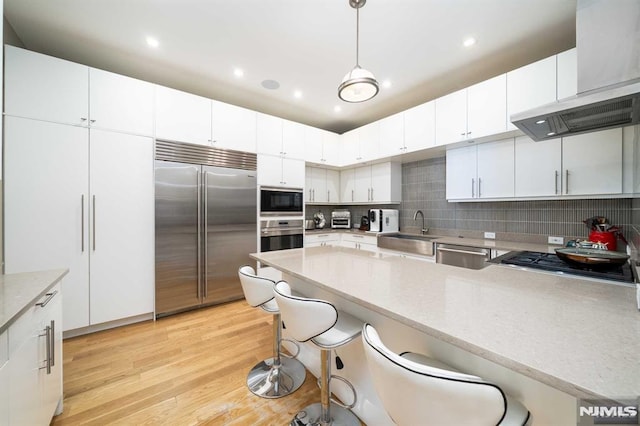 kitchen with sink, built in appliances, decorative light fixtures, white cabinets, and a kitchen bar