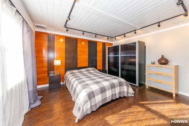 bedroom with rail lighting, wooden walls, and dark hardwood / wood-style floors