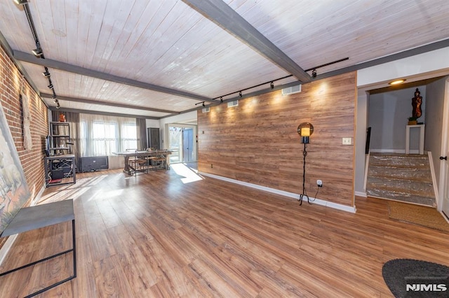 interior space with brick wall, stairway, beam ceiling, rail lighting, and wood finished floors