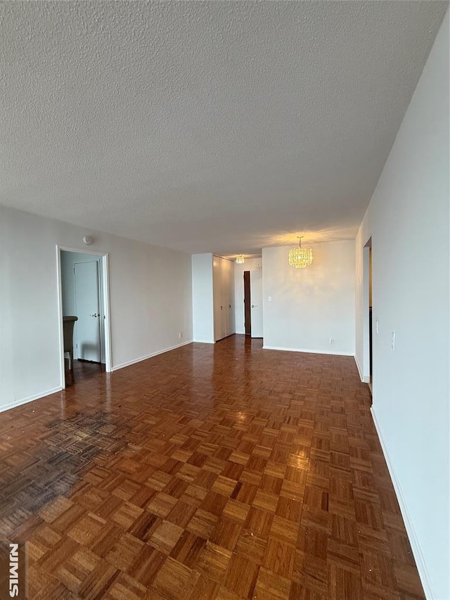 empty room with a textured ceiling, a notable chandelier, and dark parquet floors