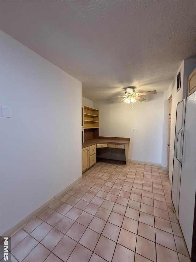 kitchen with a textured ceiling, built in desk, light tile patterned floors, white refrigerator, and ceiling fan