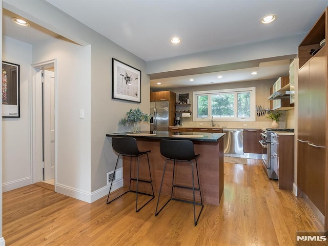 kitchen with light hardwood / wood-style floors, kitchen peninsula, sink, appliances with stainless steel finishes, and a breakfast bar area