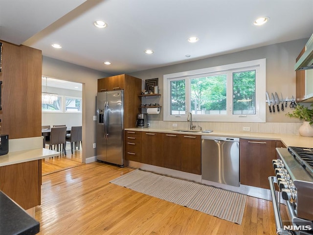 kitchen featuring wall chimney exhaust hood, sink, stainless steel appliances, and light hardwood / wood-style floors