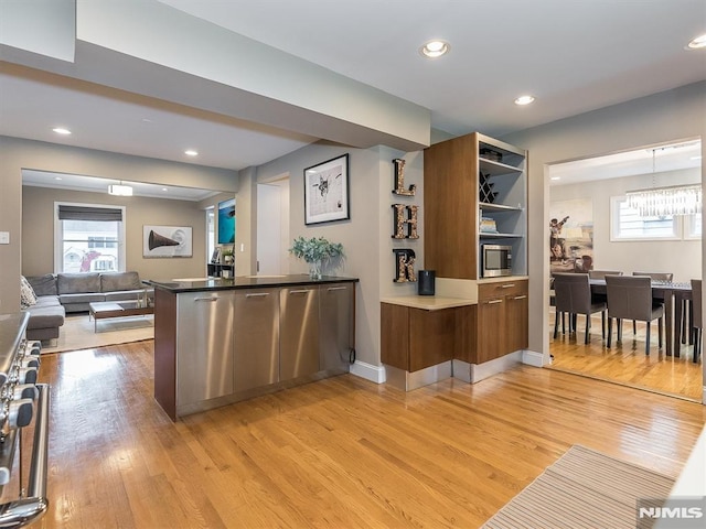 kitchen featuring pendant lighting, stainless steel appliances, an inviting chandelier, kitchen peninsula, and light hardwood / wood-style flooring