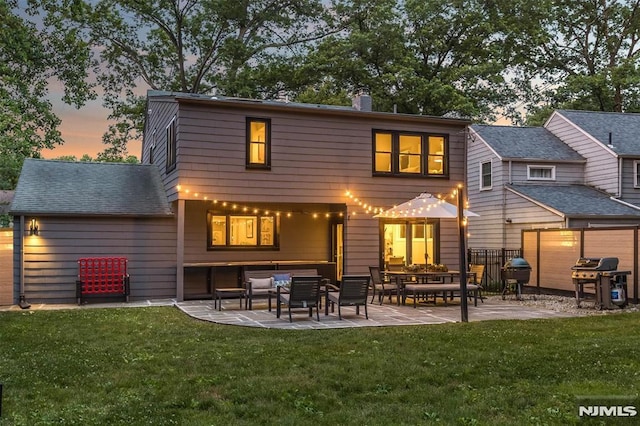 back house at dusk featuring a lawn, an outdoor hangout area, and a patio area