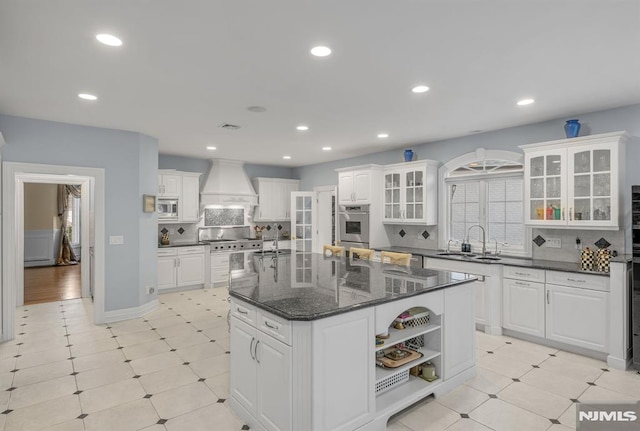 kitchen with custom range hood, decorative backsplash, a kitchen island with sink, white cabinetry, and sink