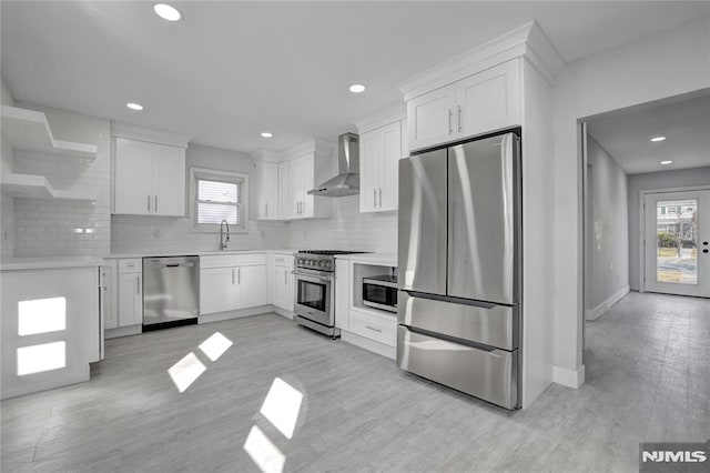 kitchen featuring stainless steel appliances, white cabinets, backsplash, and wall chimney exhaust hood