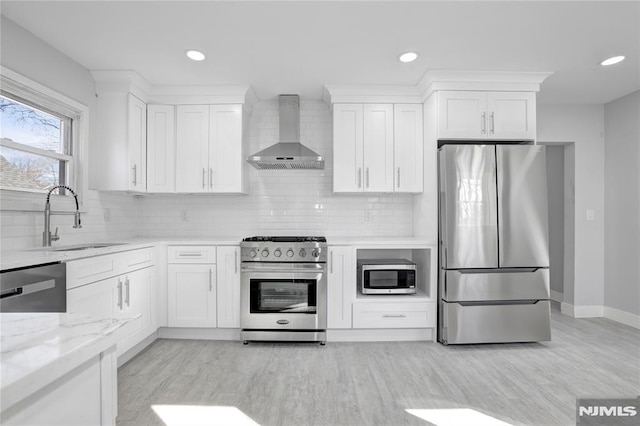 kitchen featuring appliances with stainless steel finishes, white cabinets, wall chimney range hood, and sink