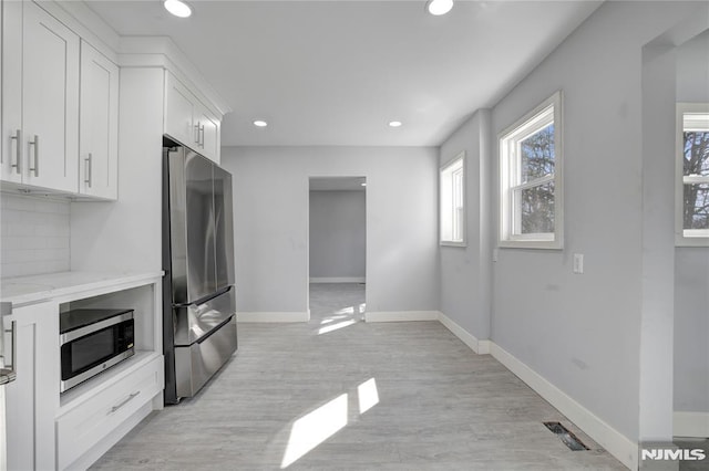 kitchen featuring white cabinetry, appliances with stainless steel finishes, light stone counters, decorative backsplash, and light hardwood / wood-style flooring