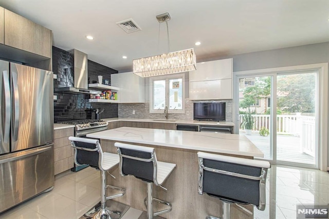 kitchen with stainless steel appliances, decorative light fixtures, a center island, wall chimney exhaust hood, and a breakfast bar