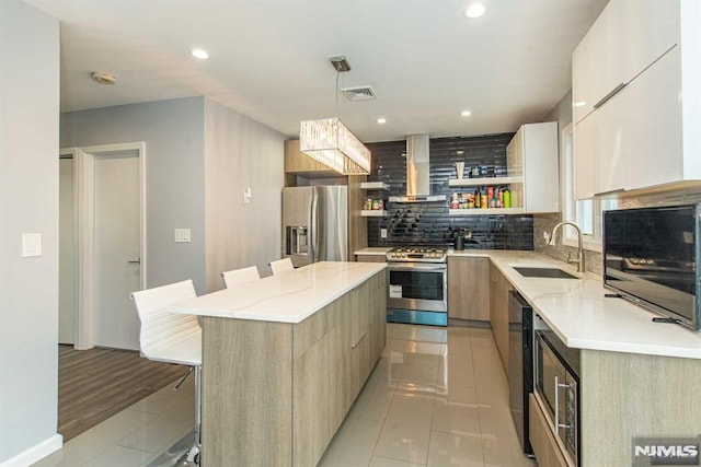 kitchen with wall chimney exhaust hood, a kitchen island, a breakfast bar area, appliances with stainless steel finishes, and sink