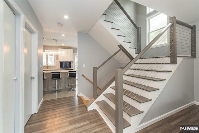 stairs featuring a notable chandelier and wood-type flooring