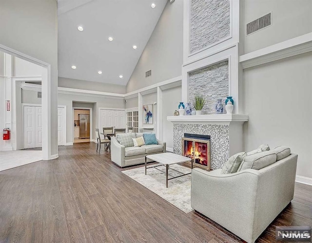 living room with high vaulted ceiling, a tiled fireplace, and wood-type flooring