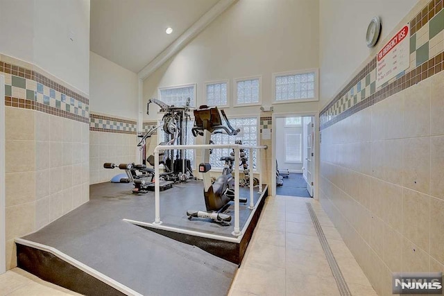 exercise area featuring high vaulted ceiling and tile walls