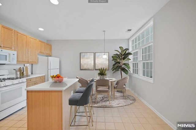 kitchen with white appliances, a center island, decorative light fixtures, light brown cabinetry, and a kitchen breakfast bar