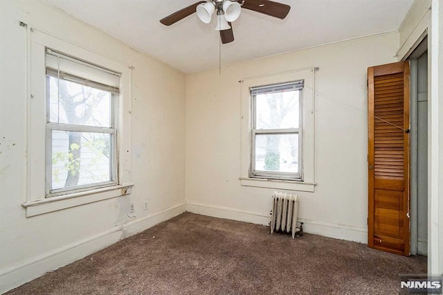 empty room with ceiling fan, dark colored carpet, and radiator