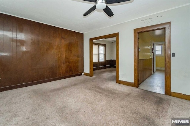 carpeted spare room featuring wood walls and ceiling fan