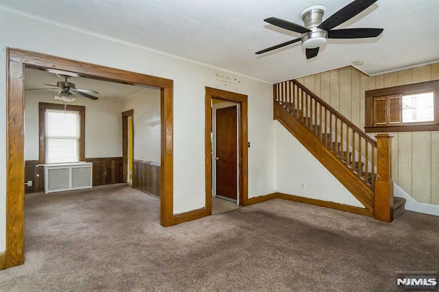 unfurnished living room with wooden walls, carpet floors, ceiling fan, ornamental molding, and radiator heating unit