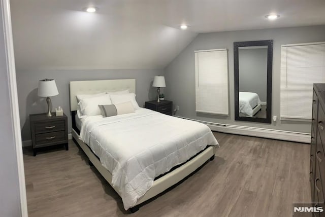 bedroom with lofted ceiling, baseboard heating, and wood-type flooring