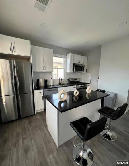 kitchen featuring stainless steel appliances, a kitchen bar, dark hardwood / wood-style flooring, white cabinets, and sink