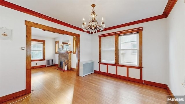 spare room featuring radiator, a fireplace, an inviting chandelier, and light hardwood / wood-style flooring