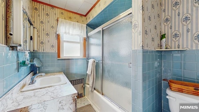 full bathroom with tile walls, radiator, toilet, bath / shower combo with glass door, and vanity