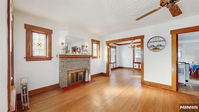 living room with ceiling fan with notable chandelier, a brick fireplace, and hardwood / wood-style flooring