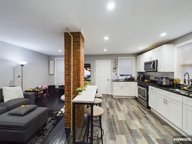 kitchen featuring stainless steel appliances, sink, white cabinetry, wood-type flooring, and backsplash