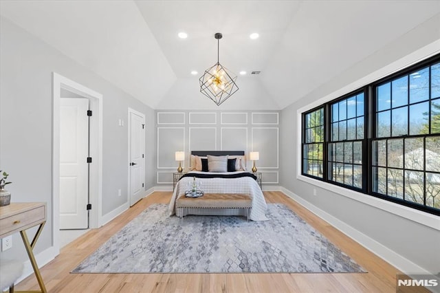 bedroom featuring baseboards, lofted ceiling, light wood-style flooring, a decorative wall, and a notable chandelier