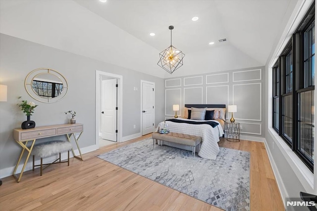 bedroom featuring lofted ceiling, recessed lighting, a decorative wall, wood finished floors, and visible vents